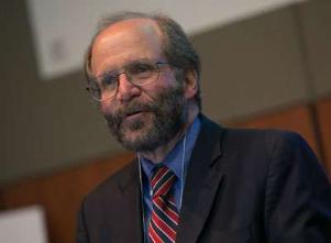 February 2024, man with balding grey hair, glasses, dark grey jacket, blue shirt, red striped tie with a partial screen and indoor green and brown wall background