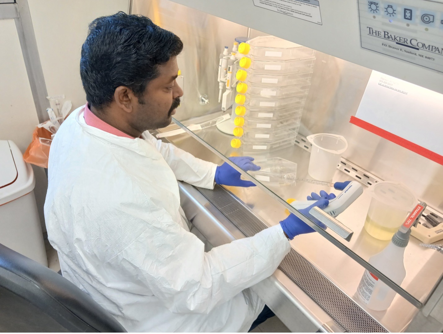 October 2024, man with dark hair and mustache wearing white lab suit with blue gloves in a lab setting