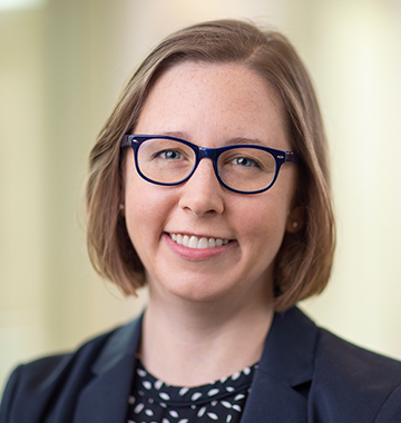 October 2024, woman with brown hair, glasses, dark jacket and polka dot shirt against a light background