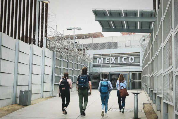 March 2024, four people walking with backpacks towards a white building with the word Mexico in white letters