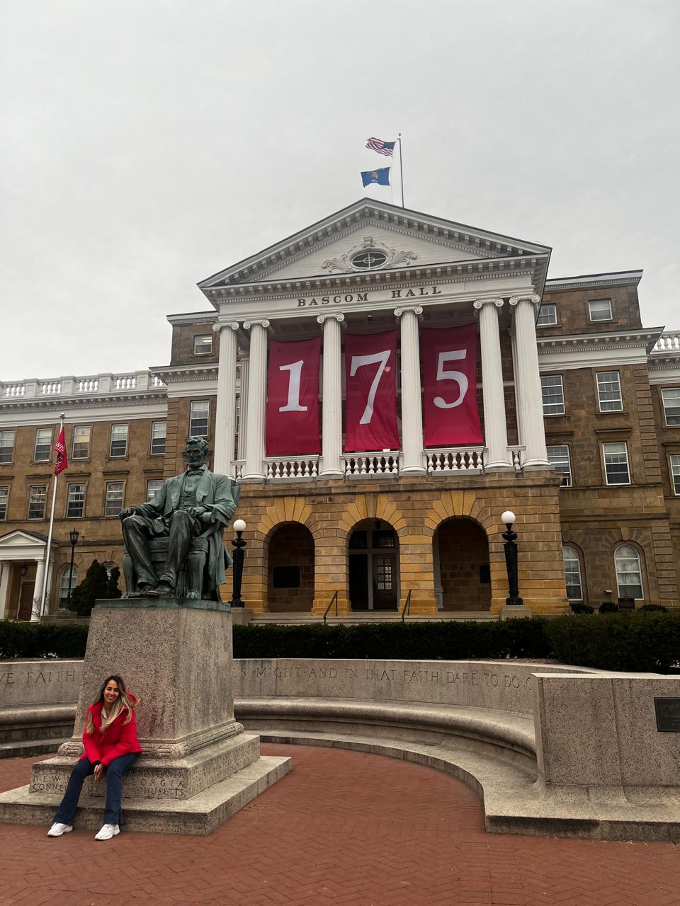 May 2024, woman sitting at a statue near Bascom Hill in Madison with 175 in red and white on the building