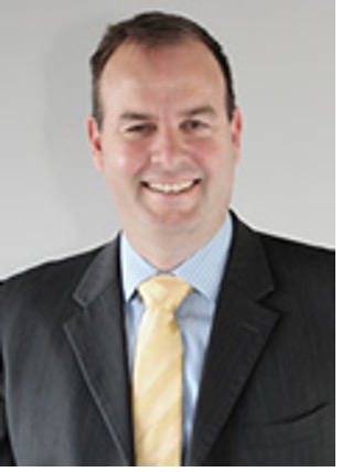 November 2024; man with dark hair, dark jacket, blue shirt and yellow tie against a light grey background