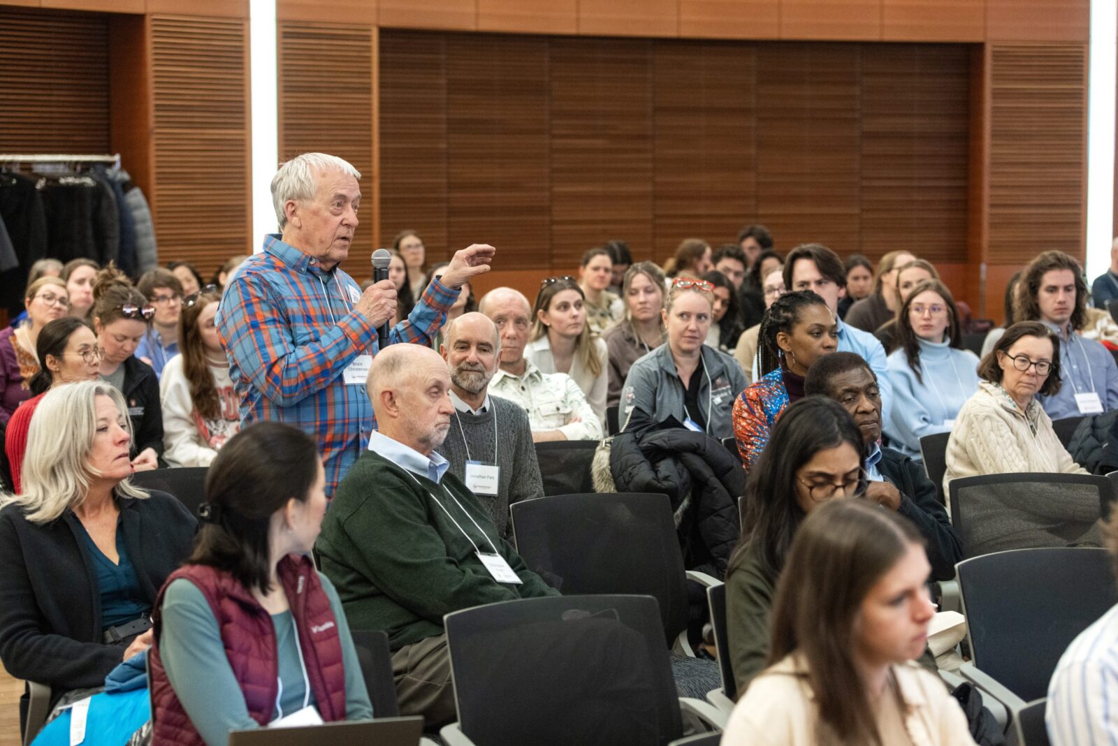April 2025 Symposium a crowd with a gentleman standing with a microphone