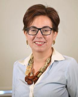 Headshot of Silvia Martins; woman with dark hair in a blue and white shirt wearing chunky necklace