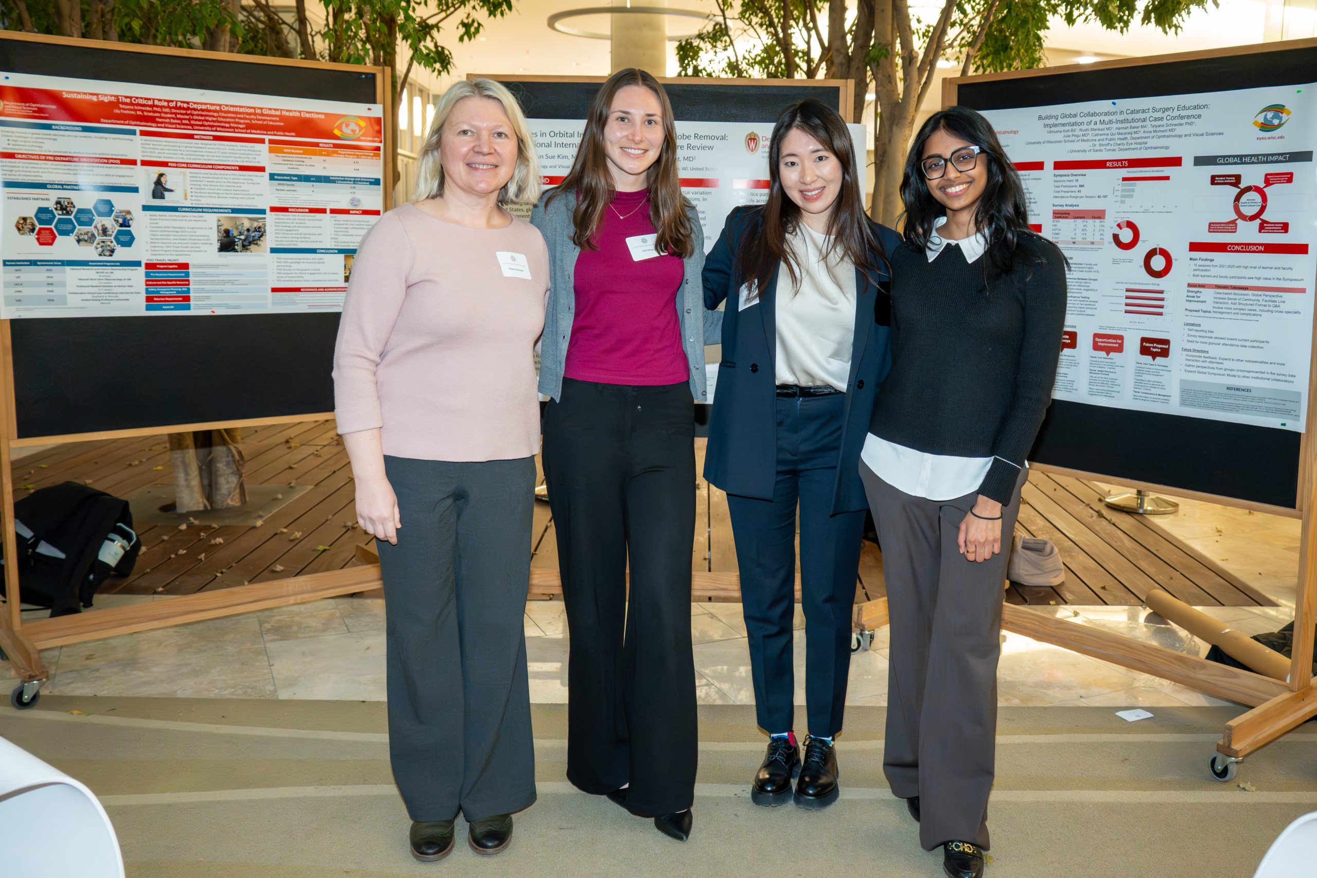 four women standing in front of poster boards in the discovery building atrium for the global health symposium