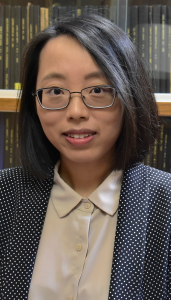 headshot of Nan Li, women with dark hair, glasses, beige top with black and white jacket against a bookshelf background