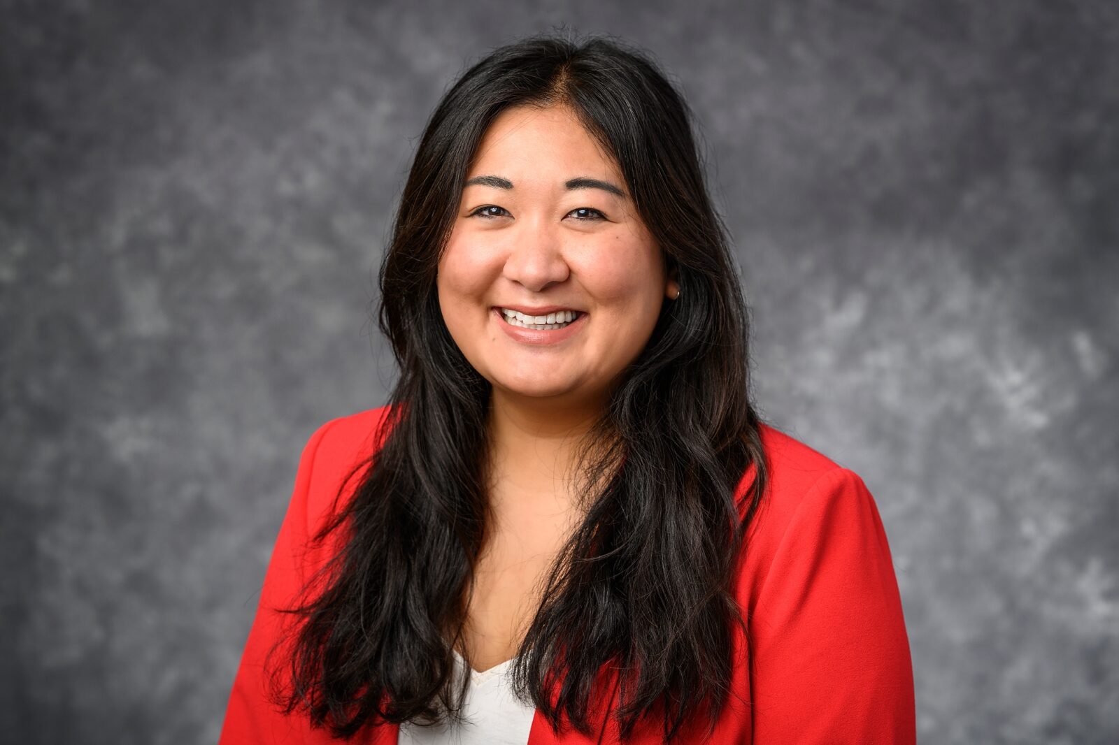 headshot of Crystal Potts, woman with dark hair, white top and red jacket against a grey background