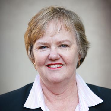 WOMAN WITH SANDY HAIR, WHITE SHIRT, DARK JACKET AGAINST A GREY BACKGROUND