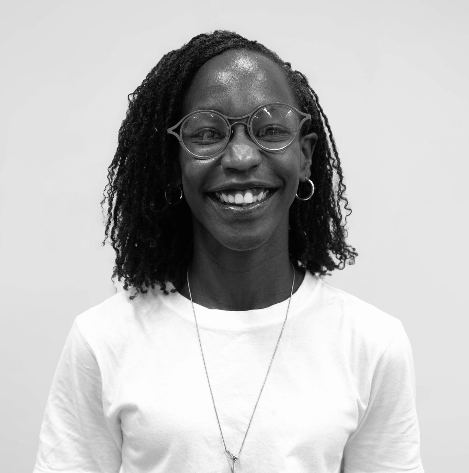 b&w headshot of Meggie Mwoka, a black woman with dark hair, glasses, a light top with necklace against a light background