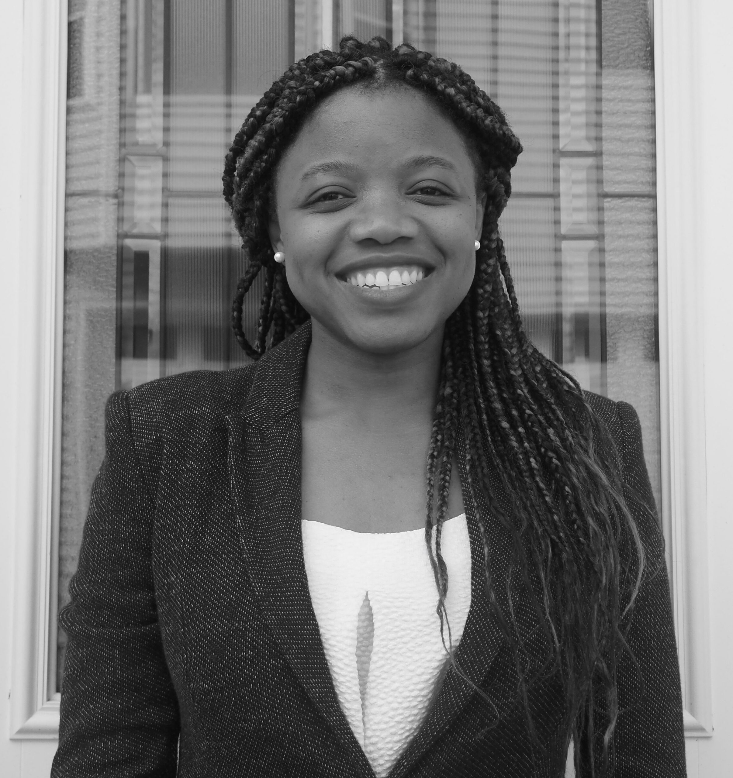 a b&w headshot of Elaine Nsoesie, a black woman with long dark hair, dark jacket and white top against a window with line reflections