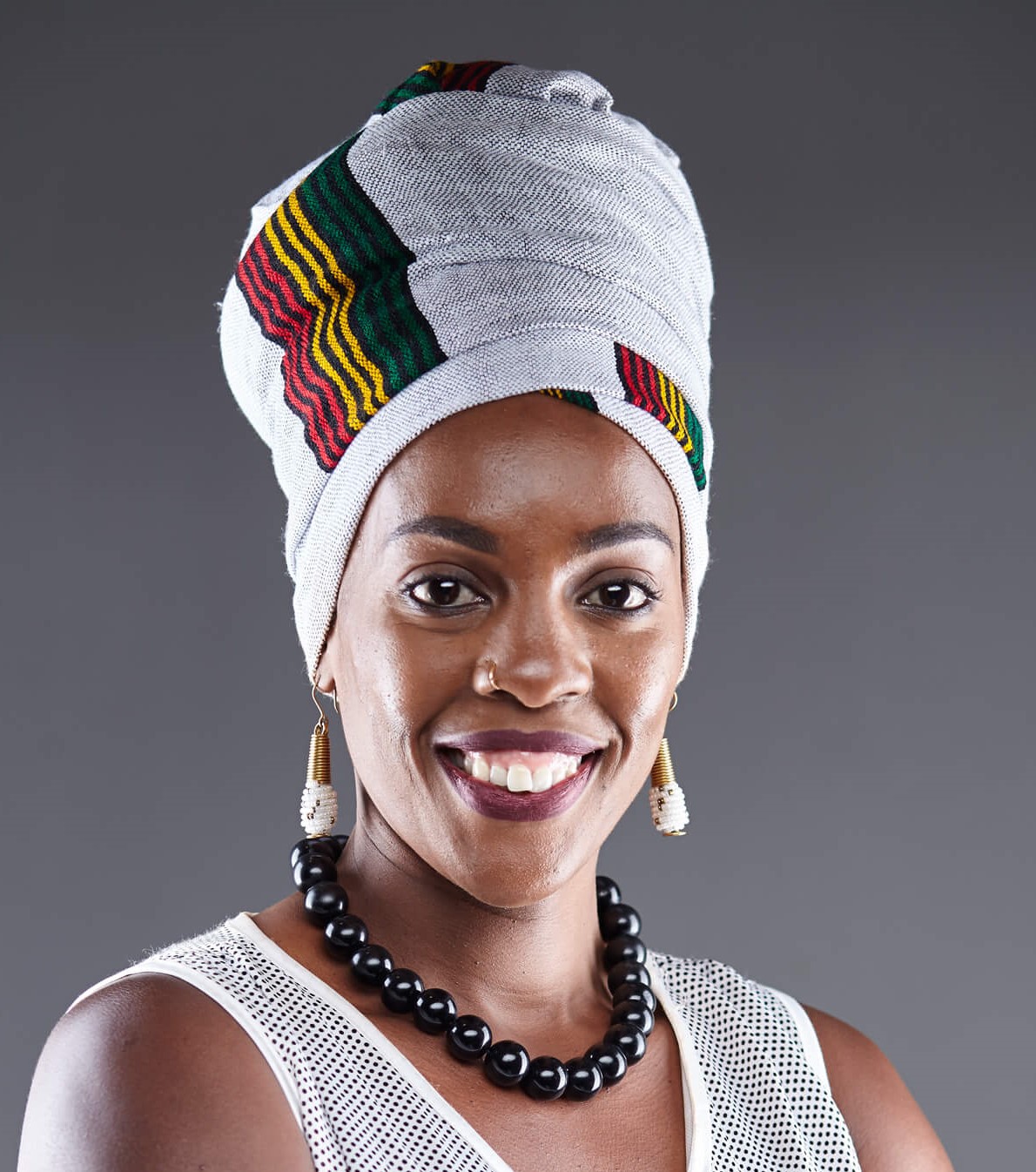 headshot of Marylene Wamukoya; black woman with white, red, yellow & green head dress with a white top against a grey background