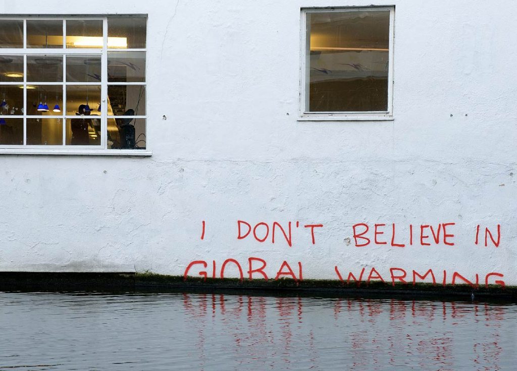Photo shows a building with floodwaters reaching up it and the words I don't believe in global warming ont he side.