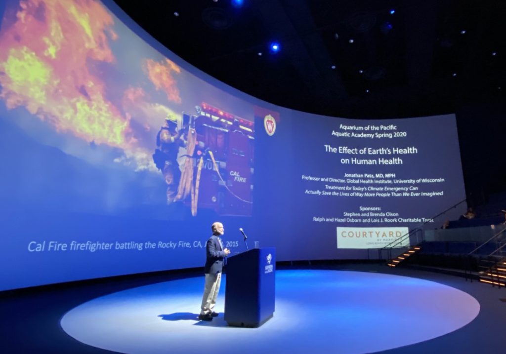 Jonathan Patz onstage with a wraparound screen behind him.