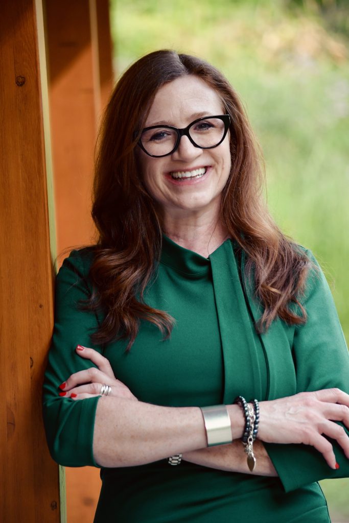 photo of woman wearing a green dress, glasses, standing outside with arms folded