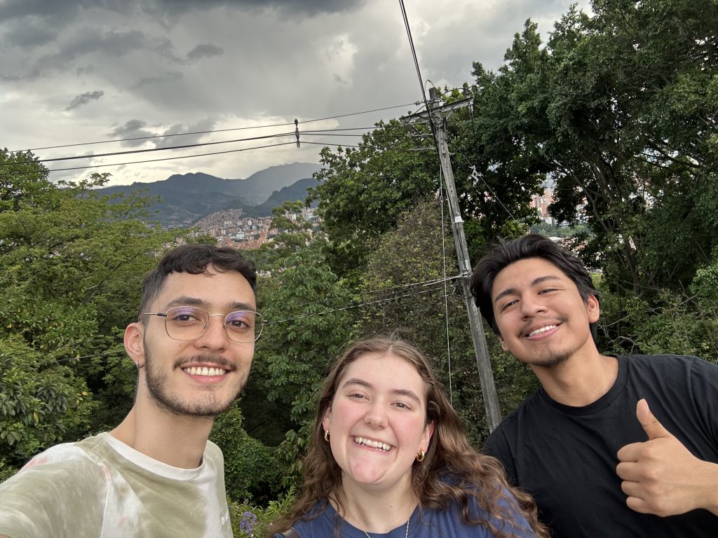 Man with green tie-dye shirt next to woman with blue shirt next to man with black shirt in front of forest background