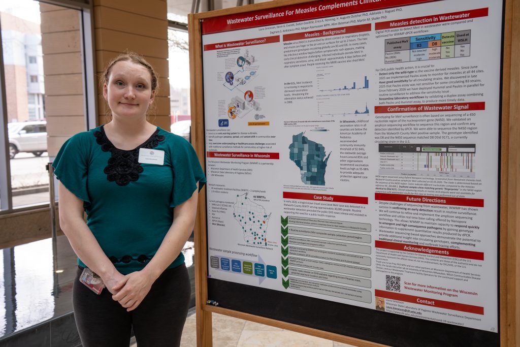 Photo from 2026 Global Health Symposium at the Discovery Building; woman in a green and black shirt standing in front of a poster in the discovery building atrium