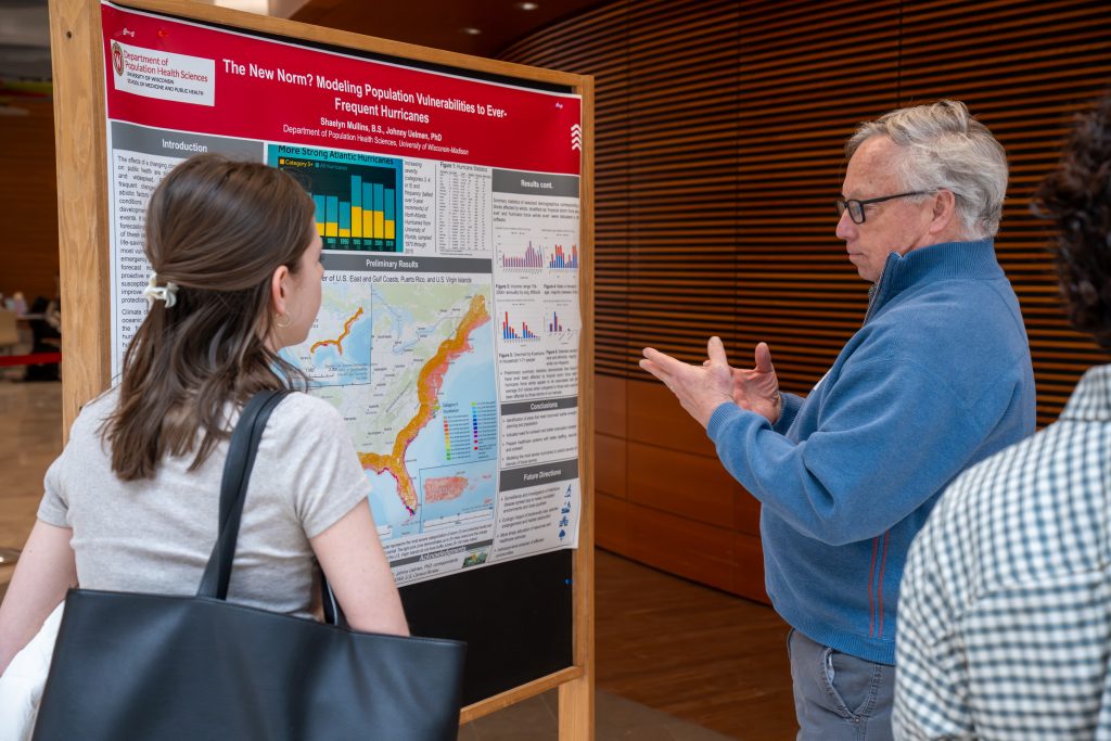 Photo from 2026 Global Health Symposium at the Discovery Building; man in a blue jacket and women with a black bag looking a poster