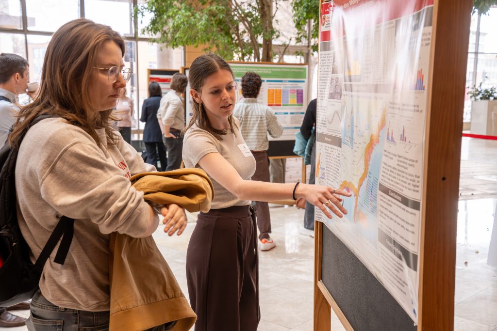 Photo from 2026 Global Health Symposium at the Discovery Building; two women standing in front of poster with one pointing