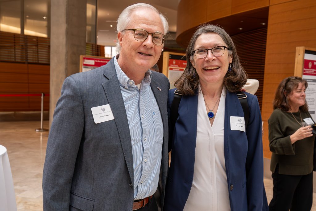 Photo from 2026 Global Health Symposium at the Discovery Building; Drs Conway and Vavrus standing and smiling with posters and students in the background