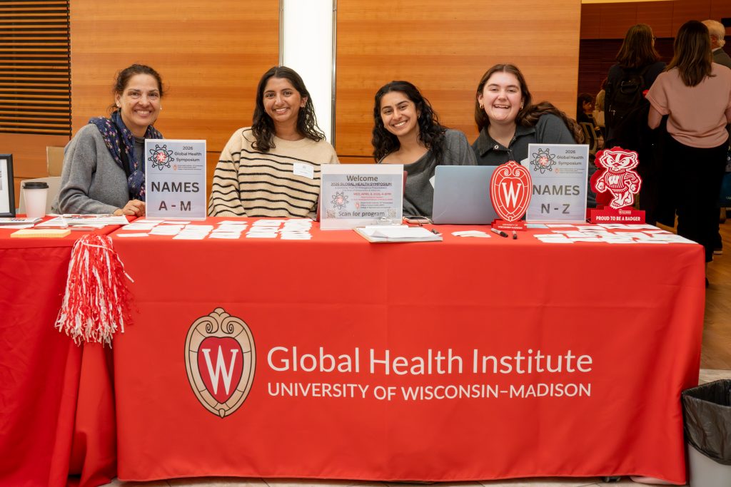 Photo from 2026 Global Health Symposium at the Discovery Building; four women sitting at the welcome desk with a red tablecloth with a UW logo