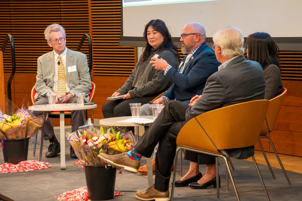 Photo from 2026 Global Health Symposium at the Discovery Building; five panelists on a stage; Dr Poulsen raised hand