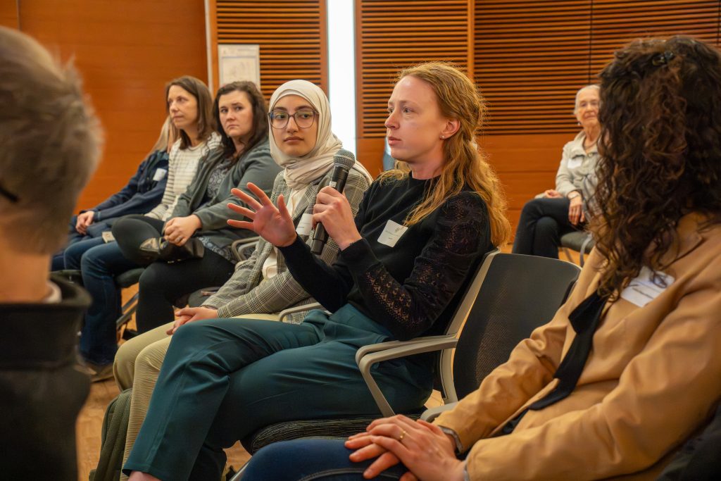 Photo from 2026 Global Health Symposium at the Discovery Building; student in a black shirt sitting with a microphone asking a question while other look on