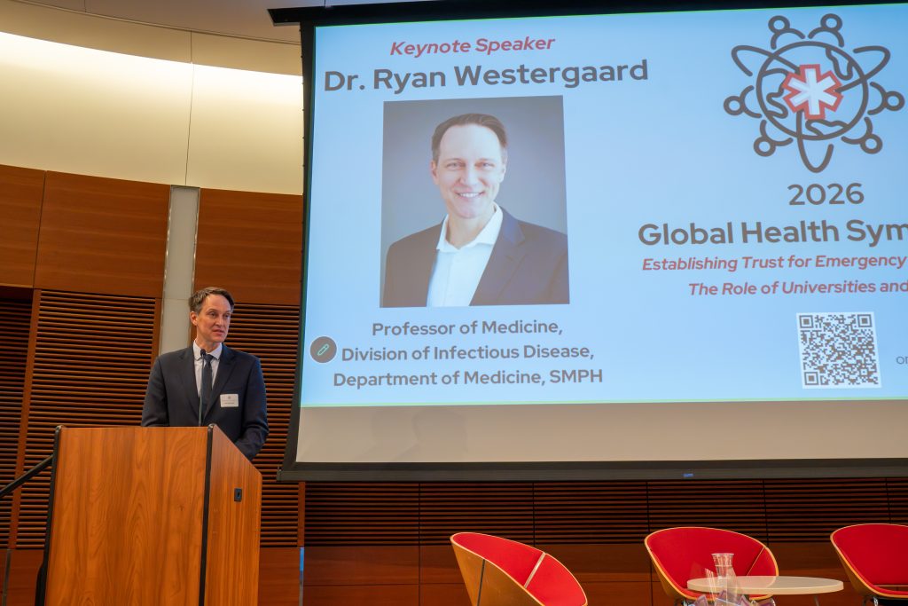 Photo from 2026 Global Health Symposium at the Discovery Building; Dr Westergaard at lectern with slide of his photo behind him