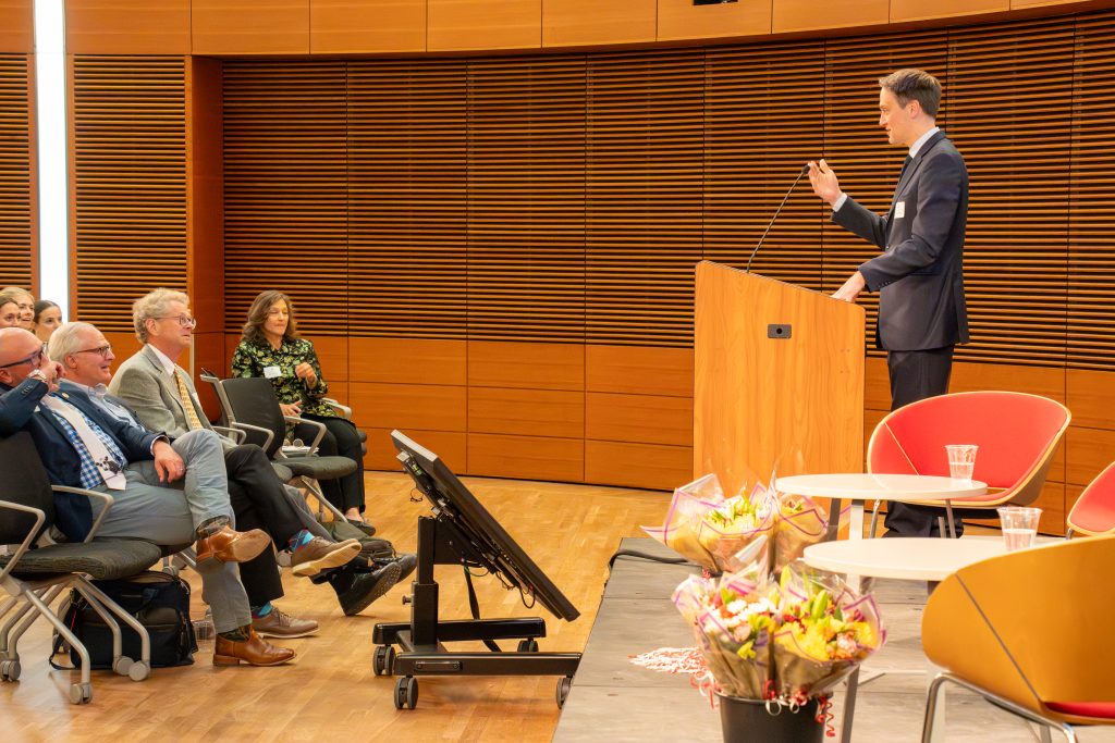 Photo from 2026 Global Health Symposium at the Discovery Building; Dr. Westergaard at lecturn with front row attendees sitting