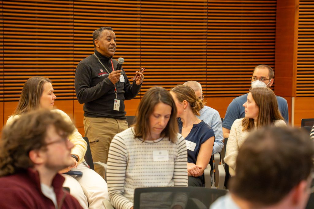 Photo from 2026 Global Health Symposium at the Discovery Building; Dawd standing and holding a microphone in the crowd