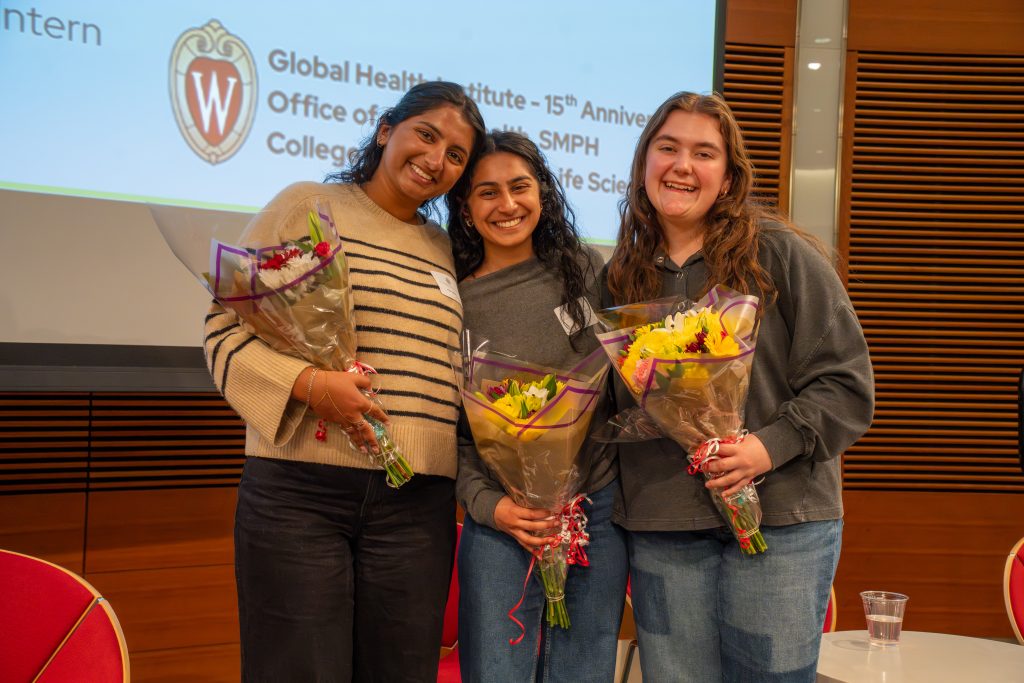 Photo from 2026 Global Health Symposium at the Discovery Building; three GHI & OGH interns holding flower bouquets on stage