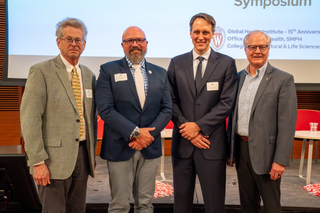 Photo from 2026 Global Health Symposium at the Discovery Building; Drs Hedberg, Poulsen, Westergaard, and Conway in front of the stage