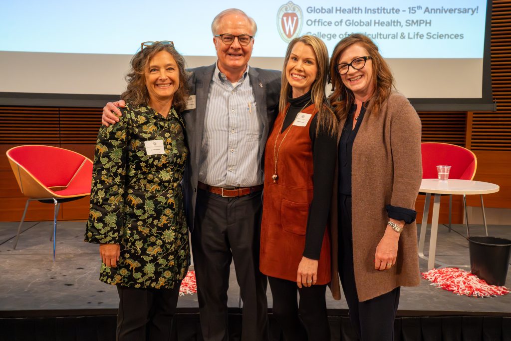 Photo from 2026 Global Health Symposium at the Discovery Building; Drs Kushner & Conway with GHI staffers Ostrowski & Newcomb standing infront of a stage