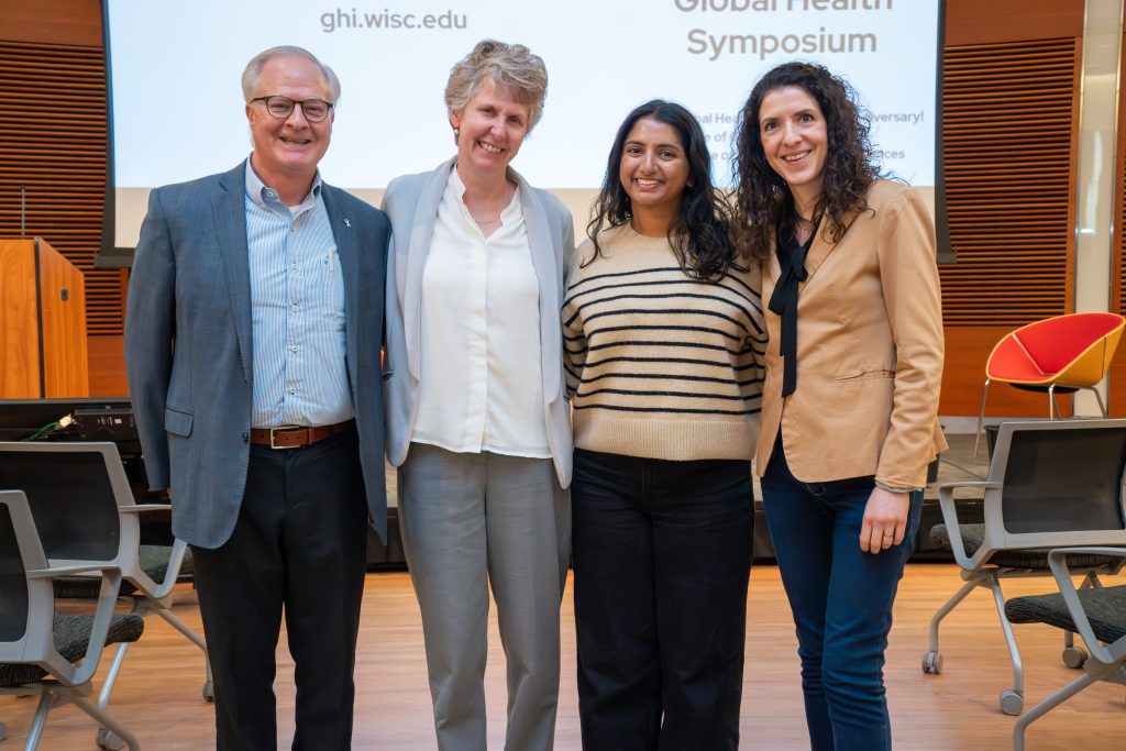 Photo from 2026 Global Health Symposium at the Discovery Building; OGH SMPH Team standing in front of stage (4 people)