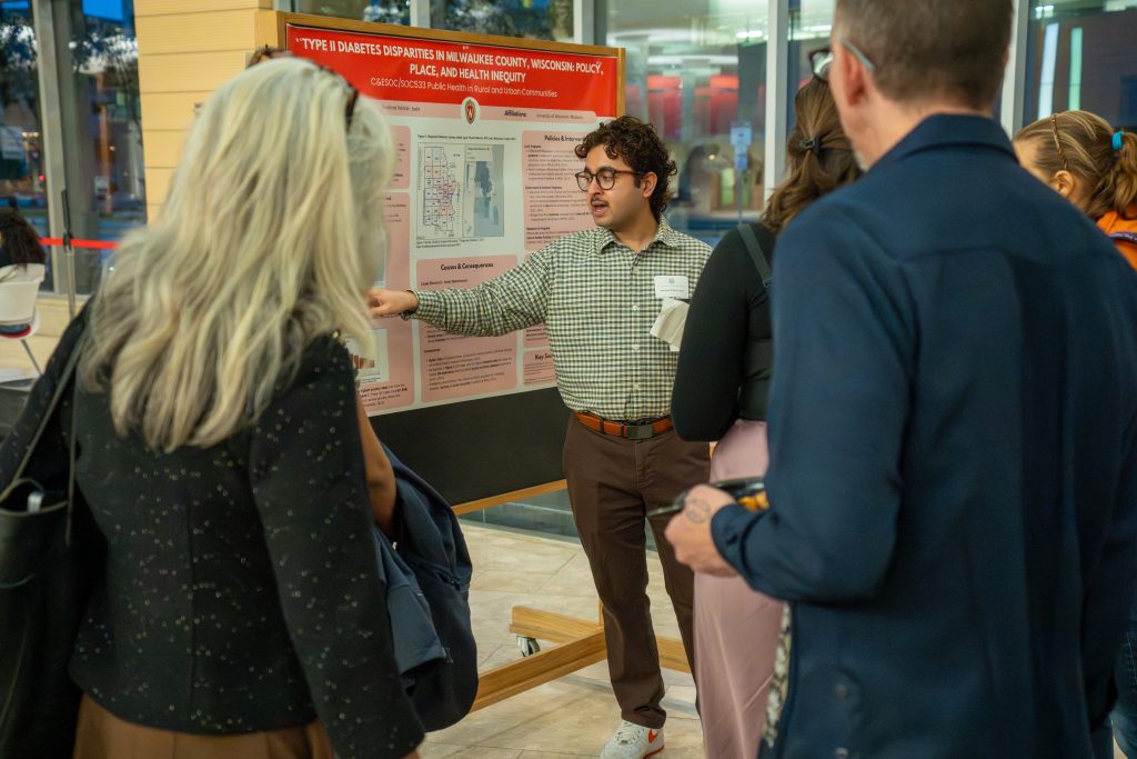 Photo from 2026 Global Health Symposium at the Discovery Building; man pointing at poster while others look on at the discovery building atrium