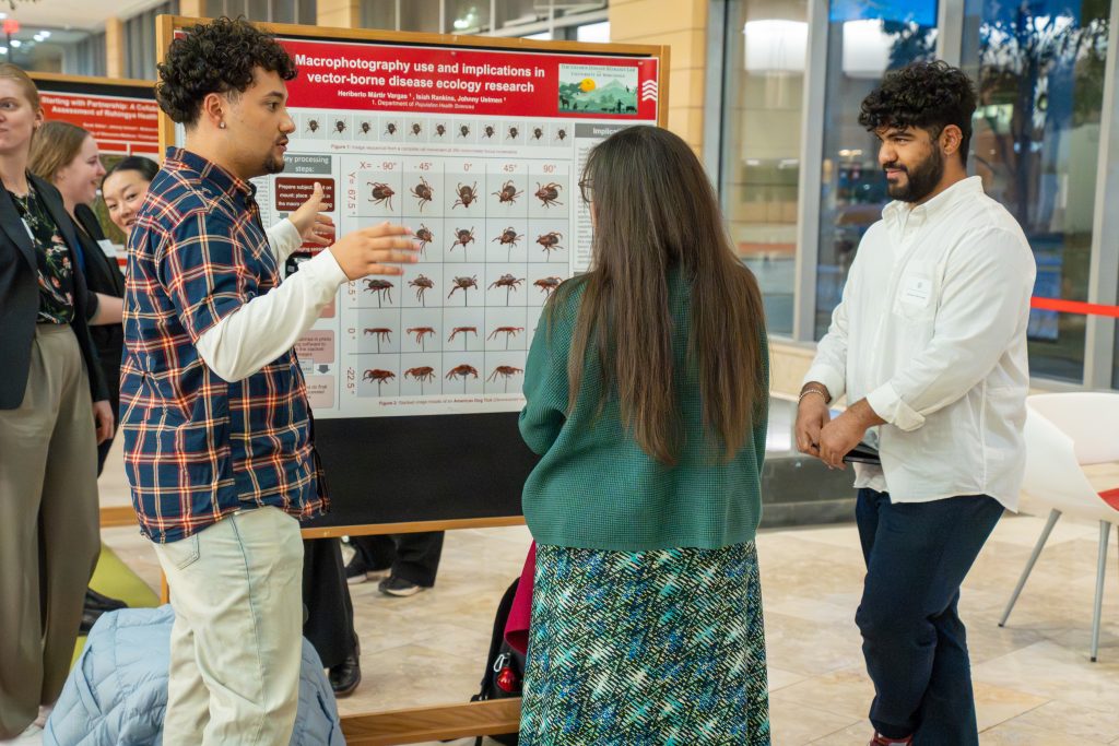 Photo from 2026 Global Health Symposium at the Discovery Building; students looking at a poster board in the discovery building atrium